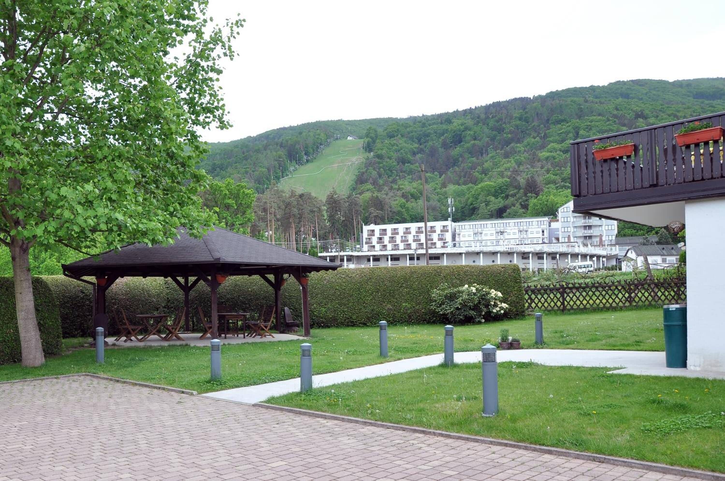 A gazebo in a landscaped area with a view of a hillside and a building in the background.
