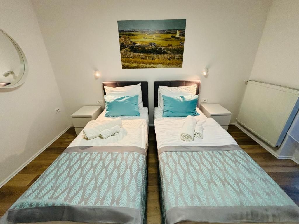 A hotel room with two beds, each with a headboard, a bedside table, and a wall-mounted picture.