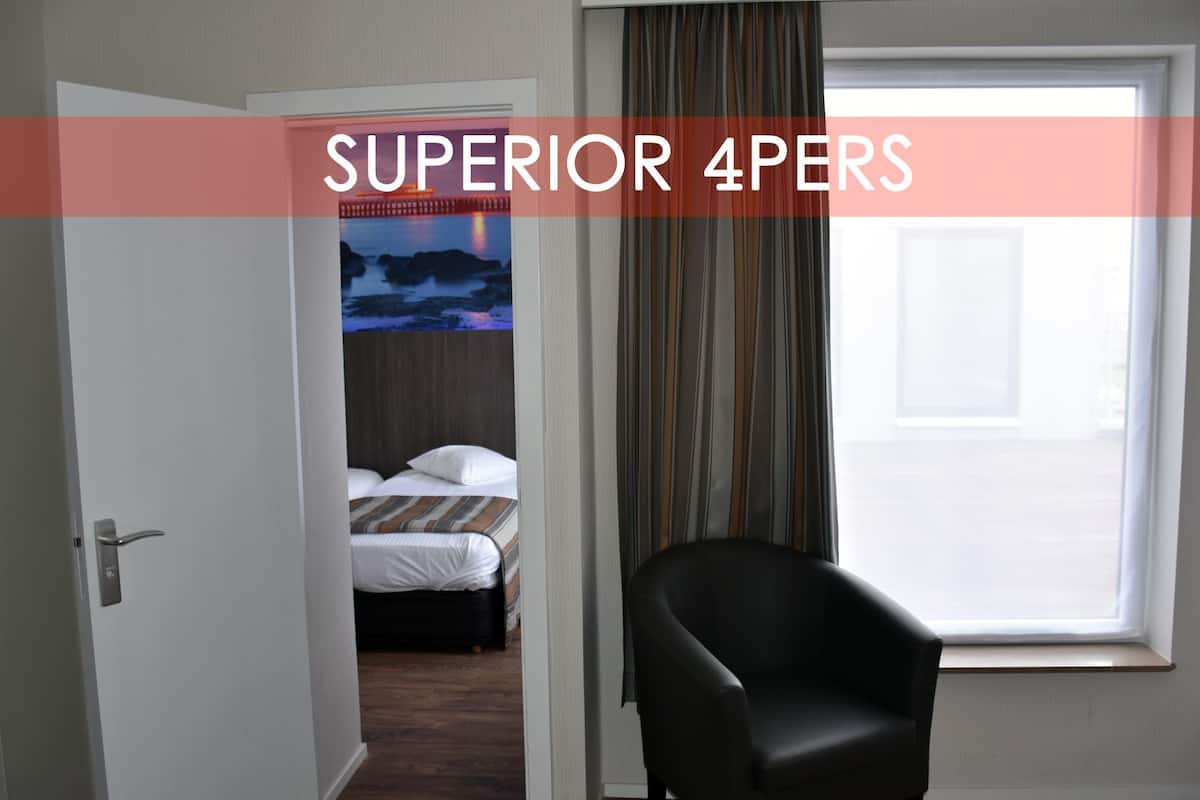 A hotel room with a bed, a chair, a window with curtains, and a door.