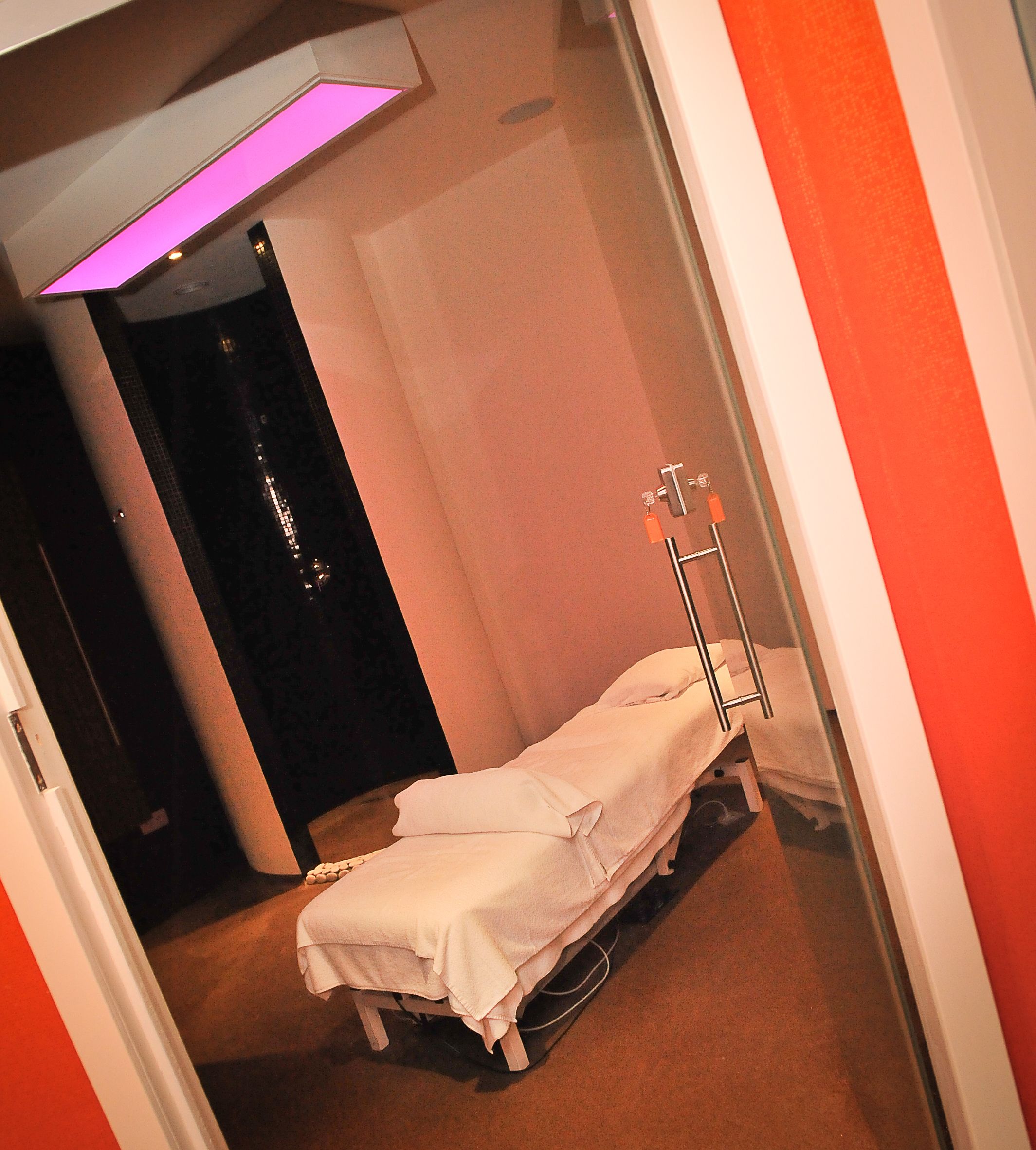 A single bed in a room with a plain wall and a door in the background.
