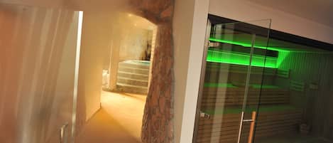 Un interior moderno con pared de piedra, puerta de cristal que da a un espacio iluminado en verde y una escalera.