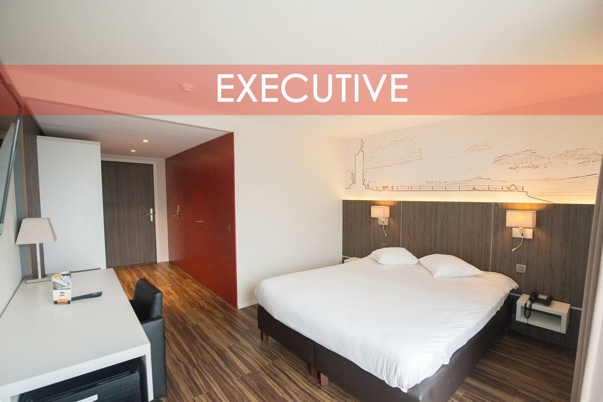A hotel room with a bed, desk, and a map on the wall.