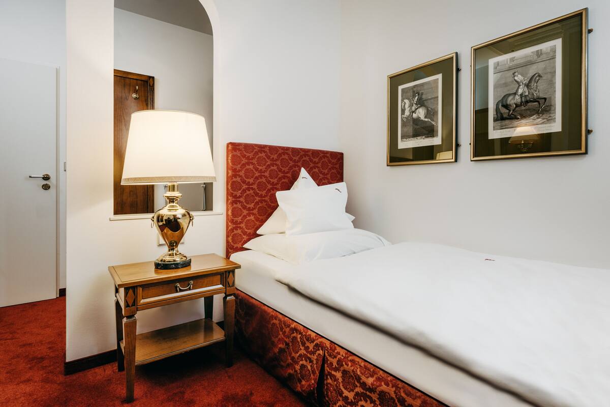 A hotel room with a bed, a nightstand with a lamp, and two framed pictures on the wall.