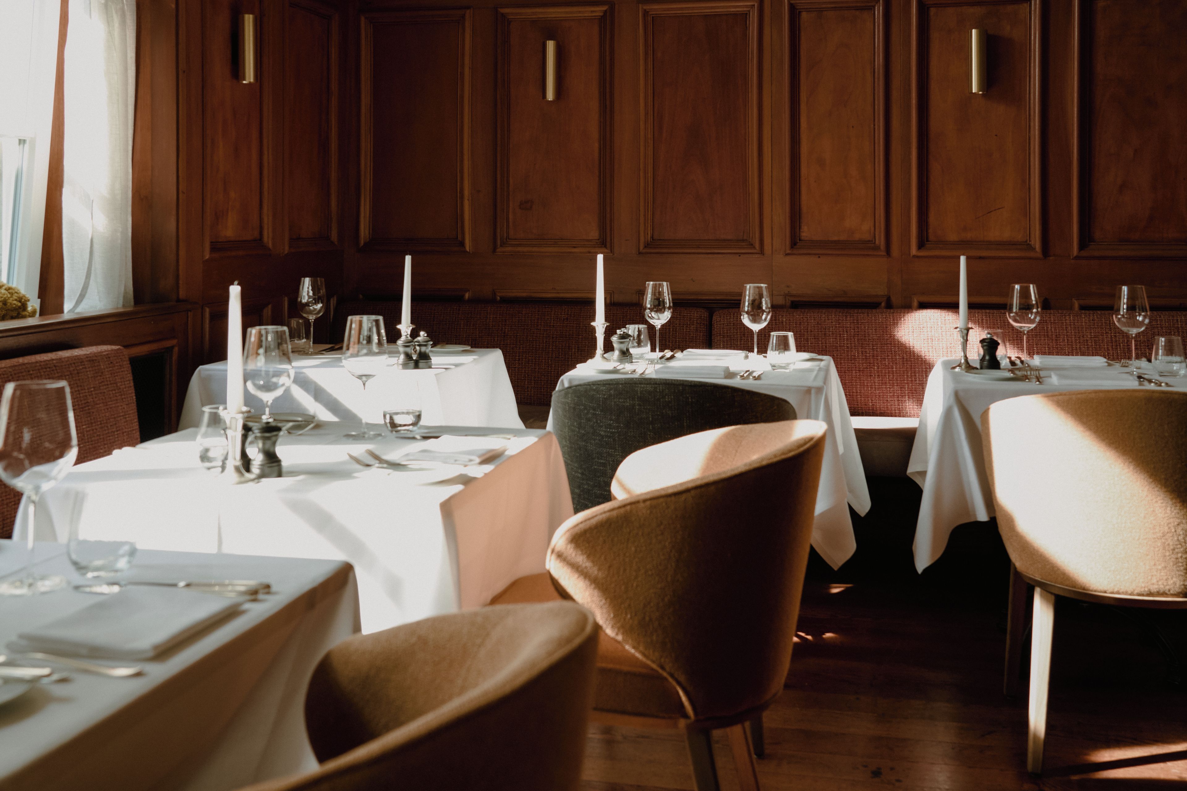 A restaurant interior with wooden paneling, white tablecloths, and candle-lit tables.