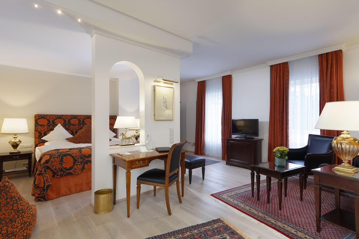 A hotel room with a bed, desk, TV, and seating area.