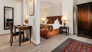 A hotel room with a wooden desk, a bed with a patterned headboard, a large mirror, and a dark wooden wardrobe. - Gebhards Hotel (Goettingen)