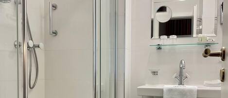 A modern bathroom with a glass-enclosed shower, a white sink with a towel, and a mirror above the sink.