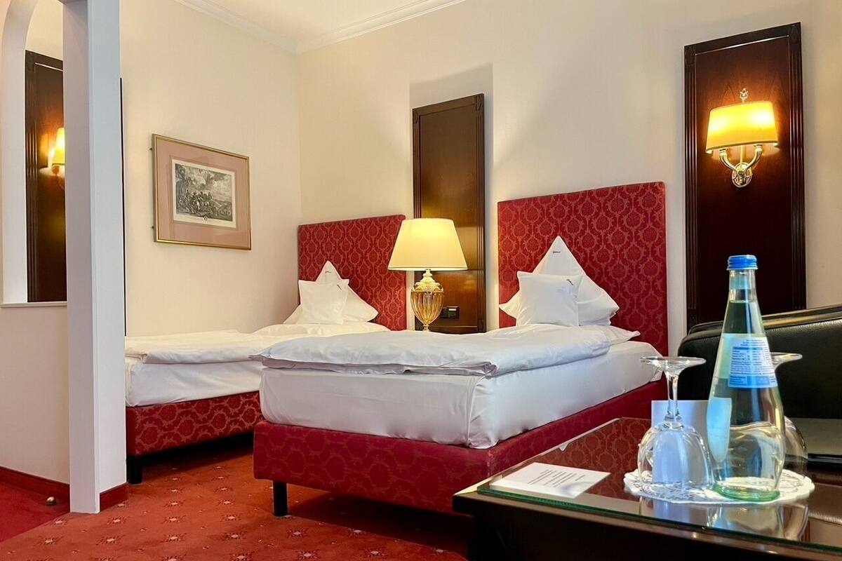 A hotel room with two beds, a desk with a lamp, a bottle, and a framed picture on the wall.