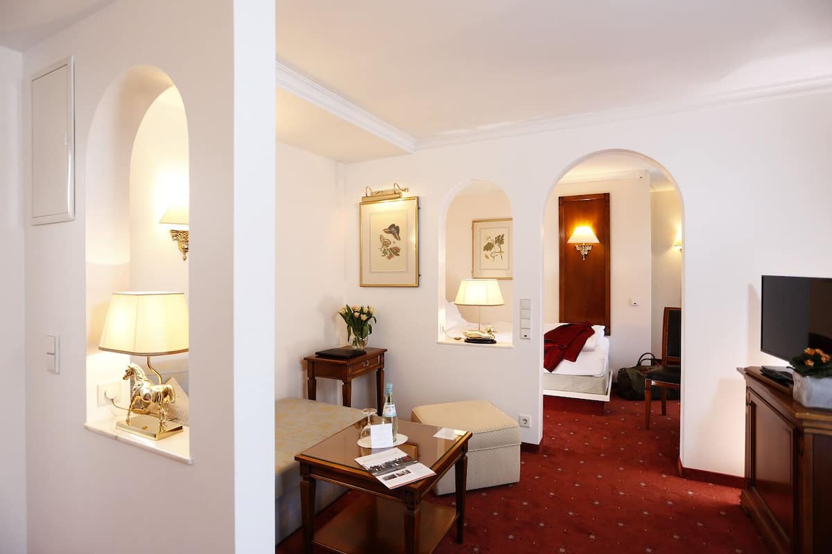 A hotel room with a red carpet, a sofa, a table with a lamp, a TV, and framed artwork on the walls.