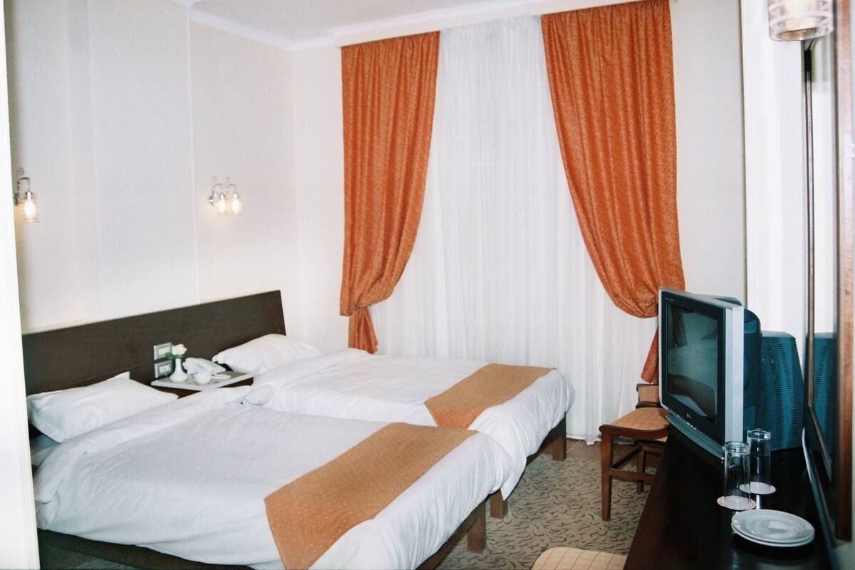 Quarto de hotel com duas camas, uma televisão e uma mesa com telefone.