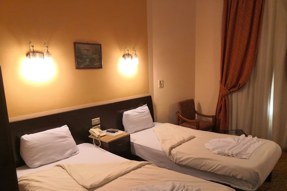 Quarto de hotel com duas camas, uma mesa de cabeceira com telefone e controle remoto, e uma cadeira.