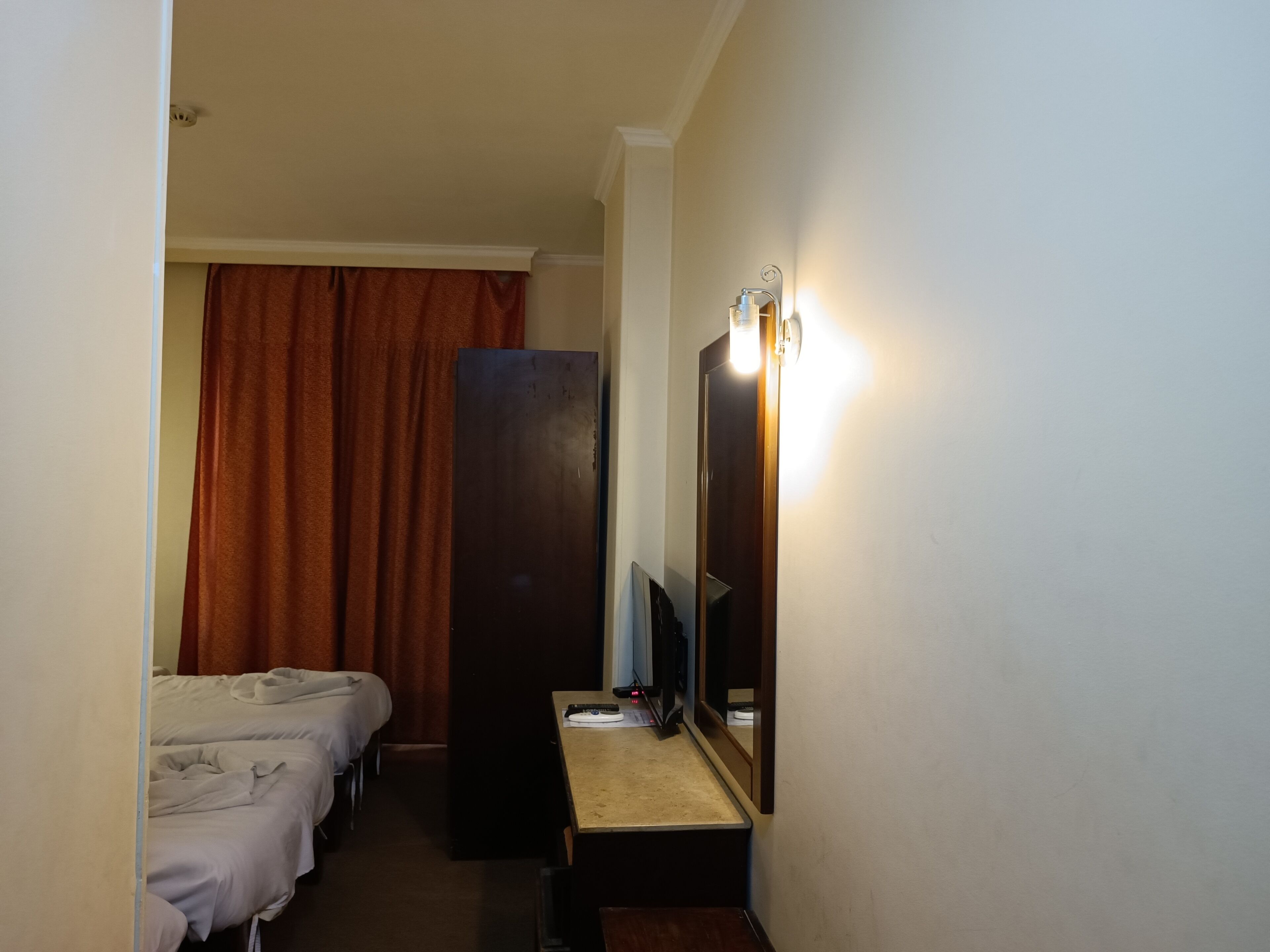 A hotel room with two beds, a desk with a mirror, and a wall-mounted light fixture.