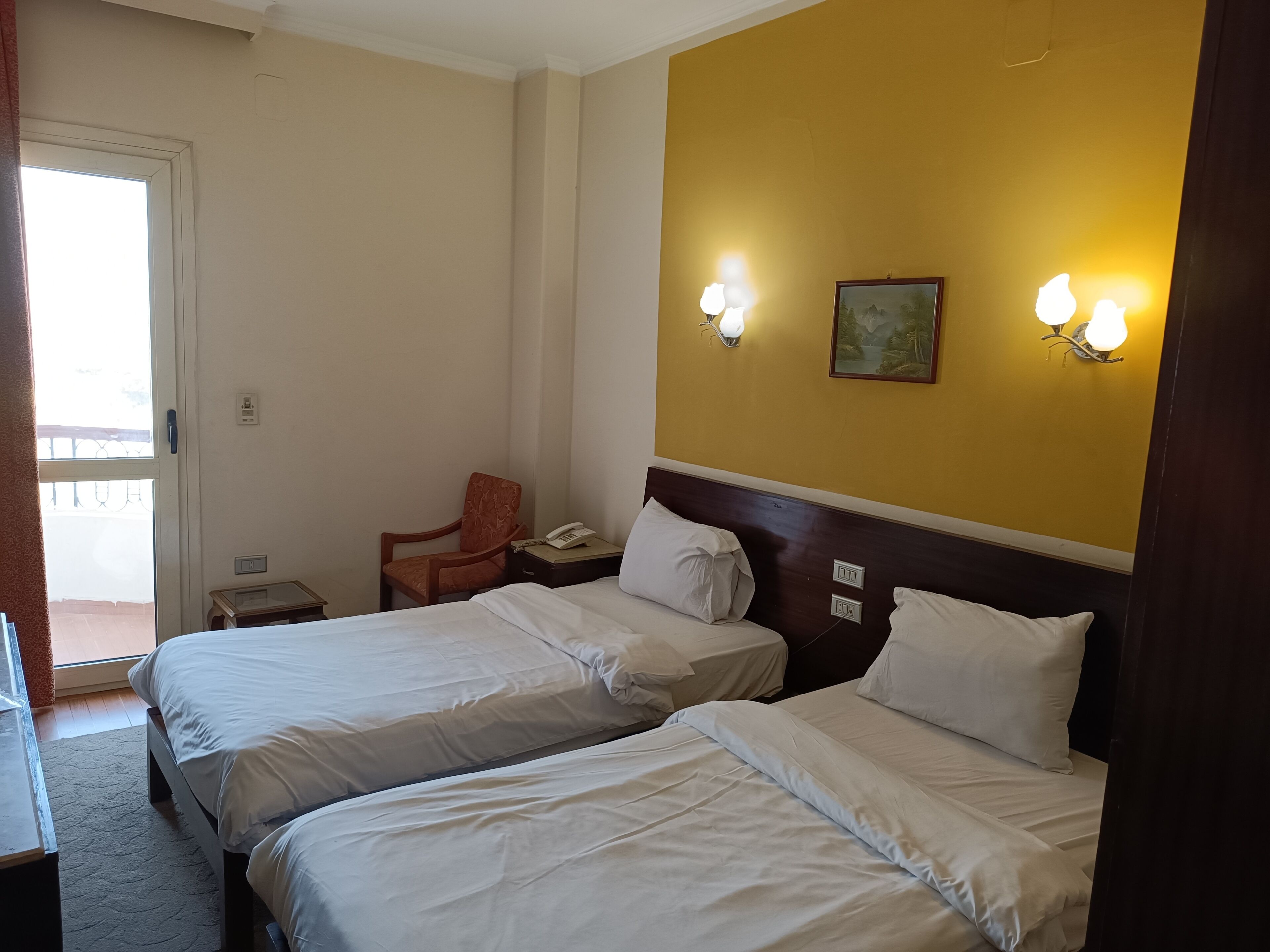 A hotel room with two beds, a chair, a desk, and a window.