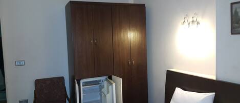 A hotel room with a bed, a wardrobe, a chair, and a wall-mounted light fixture.