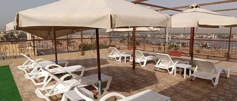 A rooftop terrace with white plastic lounge chairs and umbrellas, a green artificial turf area, and potted plants.