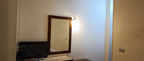 Una habitación pequeña y sencilla con escritorio, silla y espejo.