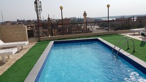 A rooftop pool with clear blue water, surrounded by a metal railing and green artificial grass. - Susanna (Luxor)