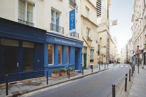 A hotel with a blue facade, a sign indicating it's a new hotel, and a street view with a pedestrian crossing. - Hôtel Bonne Nouvelle Paris (Paris)
