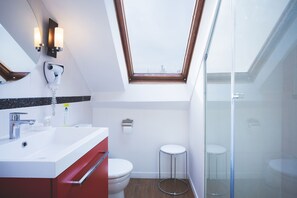 A modern bathroom with a skylight, a white sink, a red cabinet, a toilet, and a glass-enclosed shower. - Hôtel Bonne Nouvelle Paris (Paris)