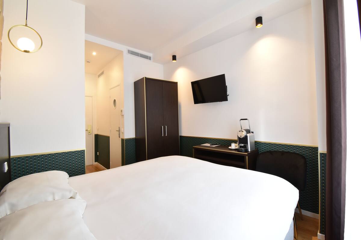 A hotel room with a bed, a desk, a chair, a television, and a wardrobe.