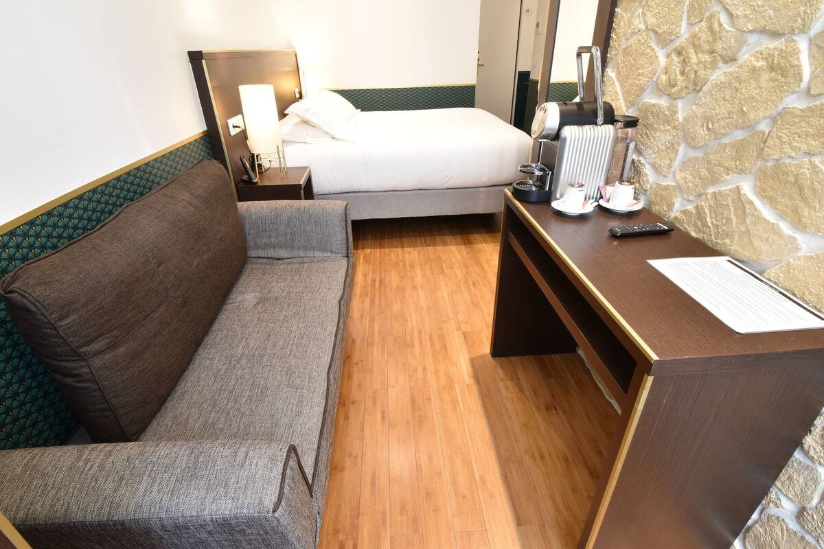 A hotel room with a bed, a desk, a chair, and a sofa.