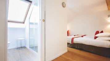 Un dormitorio con cama, un taburete pequeño y un tragaluz.