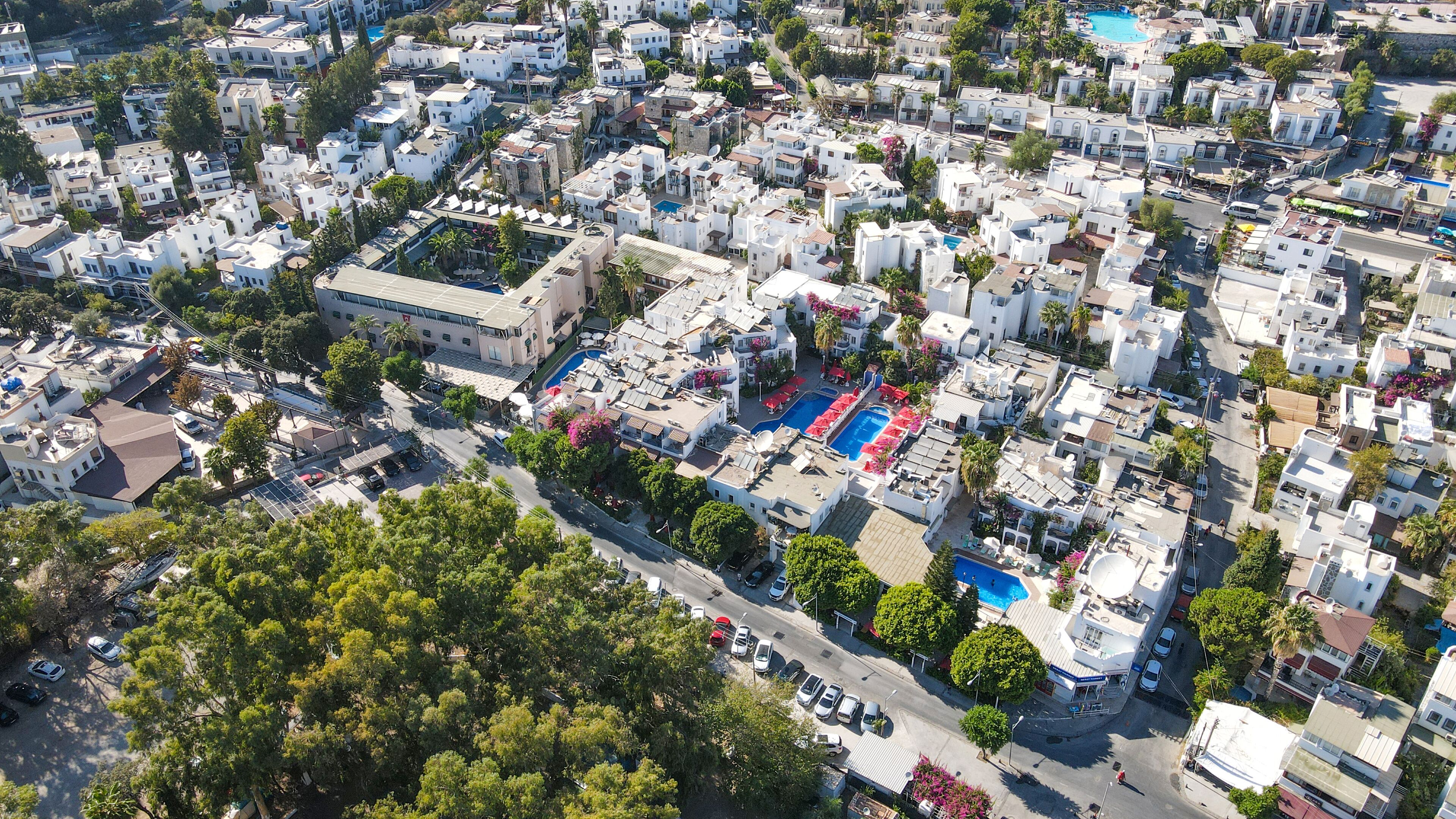 An aerial view of a densely packed urban area with white buildings, a central swimming pool, and surrounding greenery.