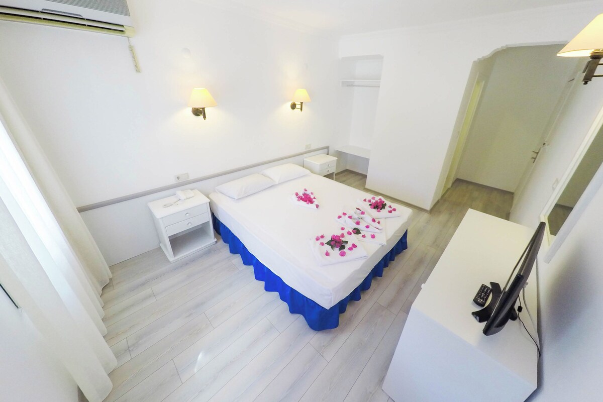 Una habitación de hotel con cama, mesitas de noche, escritorio y televisor.