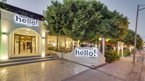 Entrada de hotel con un llamativo cartel que dice 'hello!', un área de estar al aire libre cubierta y una fachada bien iluminada.