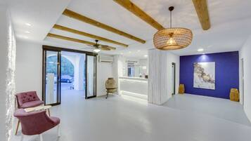 A spacious room with a white floor, a ceiling fan, a woven light fixture, a reception desk, and a large window with a view of a car outside.
