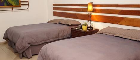 A hotel room with two single beds, a wooden headboard, a bedside table with a lamp, and a small potted plant.