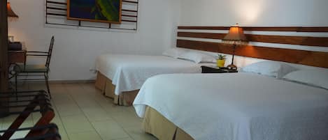 Habitación de hotel con dos camas individuales, cabecera de madera, mesita de noche con lámpara, una silla, un cuadro en la pared y una pequeña planta en maceta.