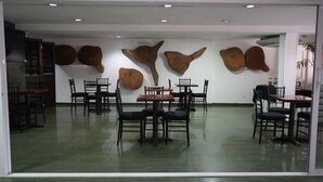 Restaurante com várias mesas e cadeiras, piso de azulejos verdes e objetos decorativos fixados na parede.