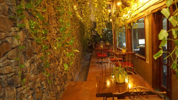 Um espaço acolhedor ao ar livre, com paredes de pedra e vegetação, com mesas e cadeiras.