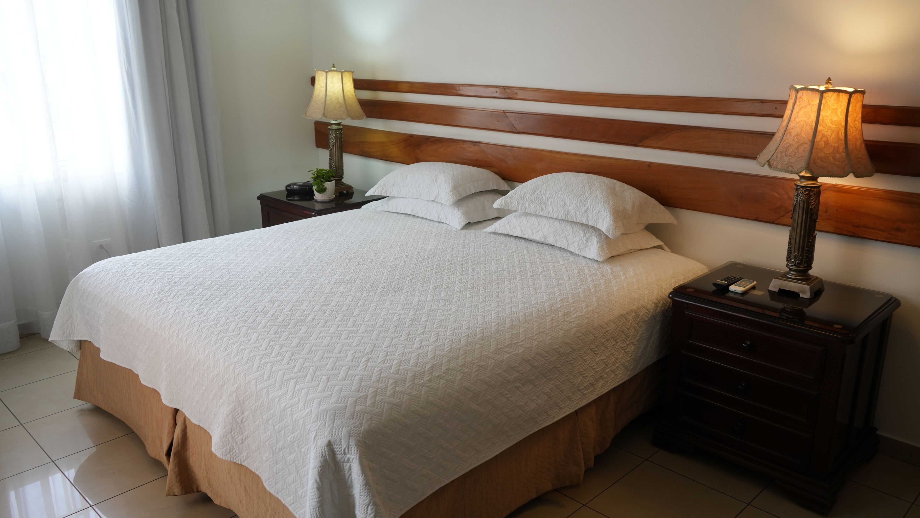 A neatly made bed with a white quilt, two bedside tables with lamps, and a wooden headboard.