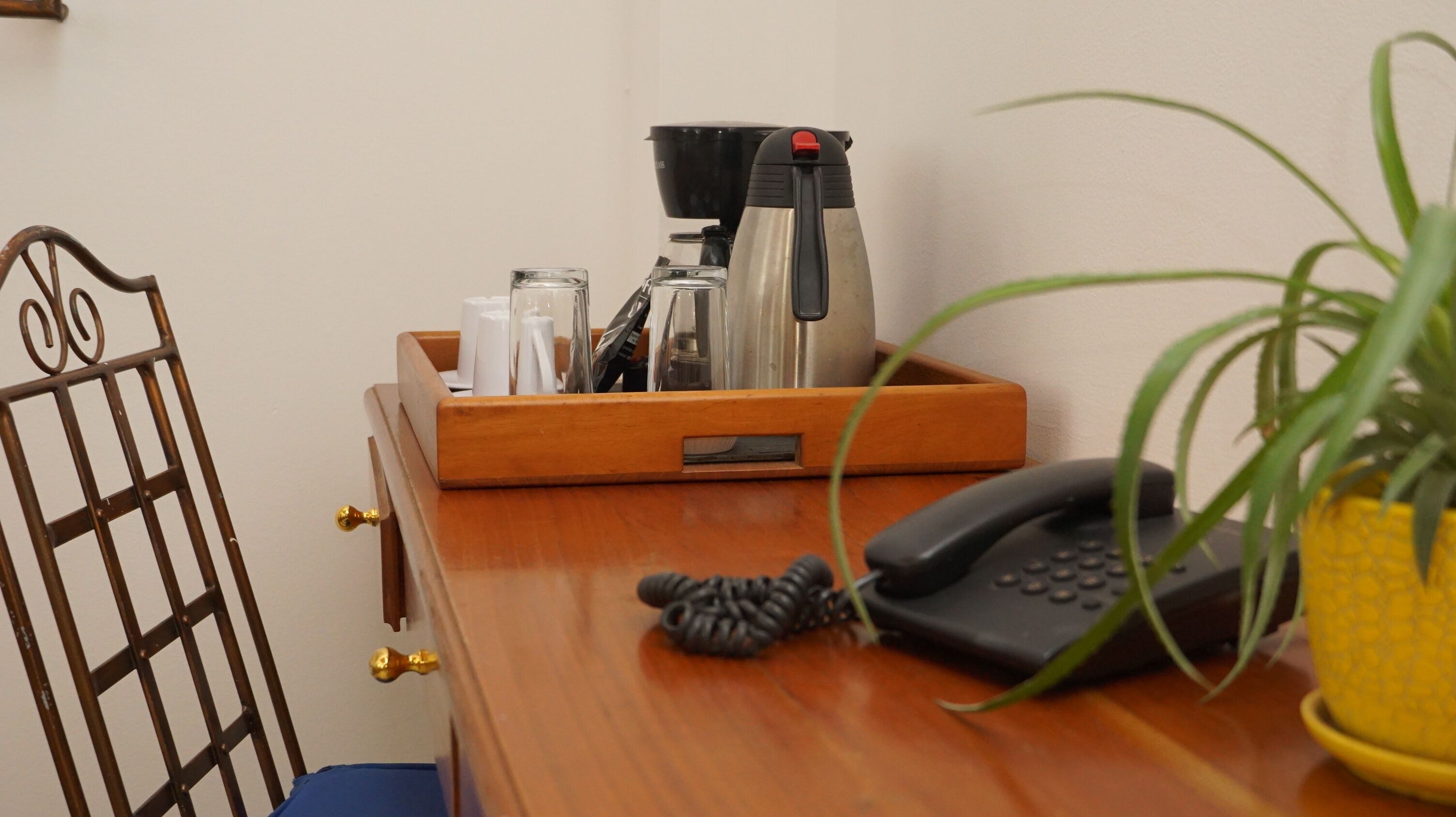Een houten bureau met een koffiezetapparaat, een telefoon en een kamerplant.