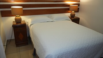 Una cama bien hecha con cabecera de madera, dos lámparas de noche y una mesita de noche de madera con una lámpara.