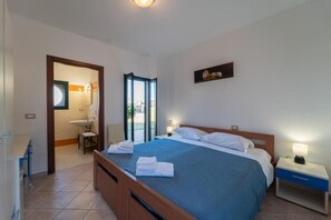 Habitació d'hotel amb llit, taula de nit i vista a l'exterior per una porta de vidre.