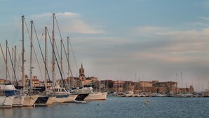 A marina with multiple sailboats docked, a prominent church with a bell tower, and a coastal town in the background.