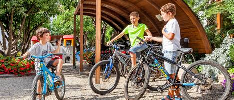 A covered bike area with multiple bicycles and a small building in the background.