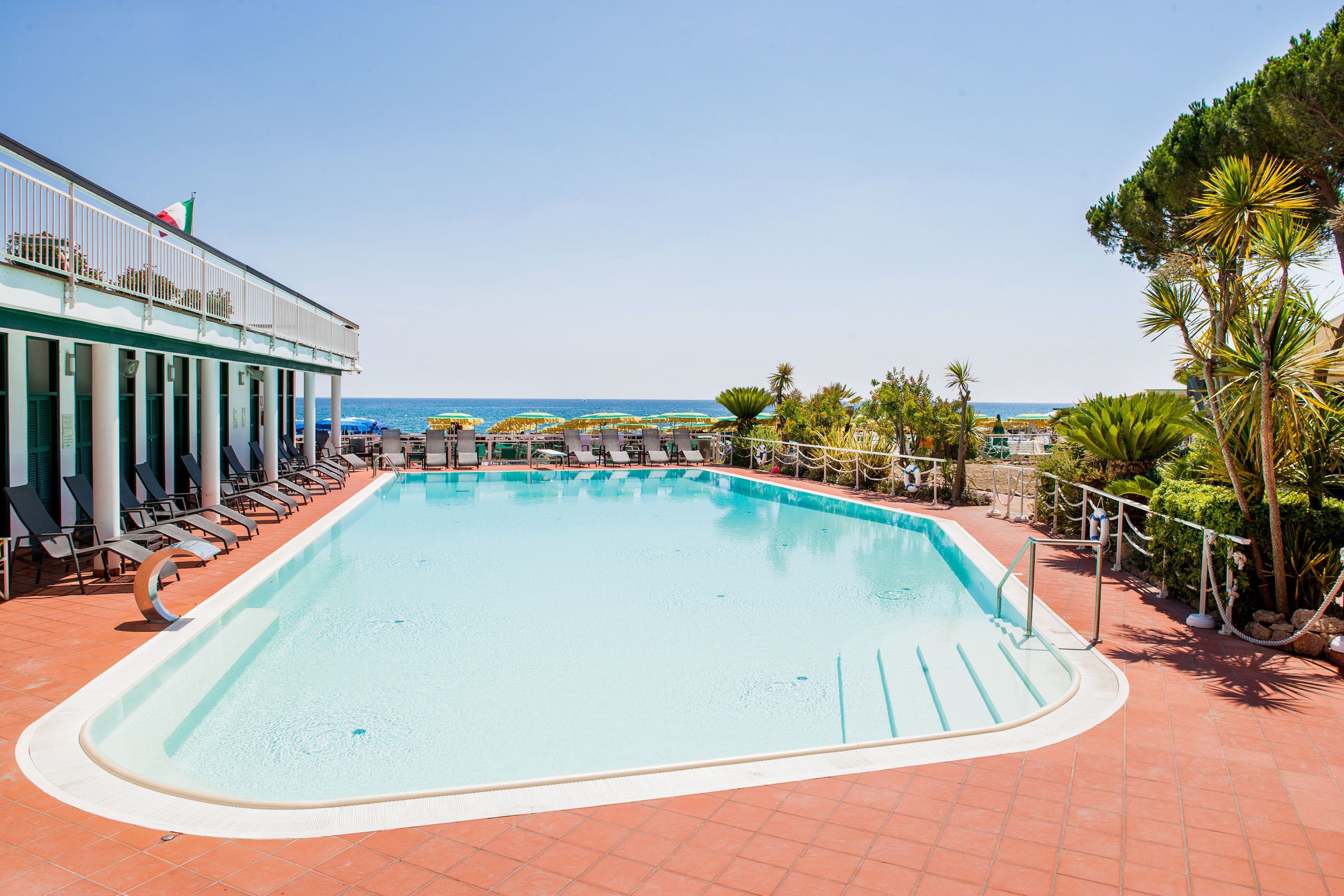 Une piscine entourée de palmiers, avec des chaises longues et des parasols, offrant une vue sur la mer.