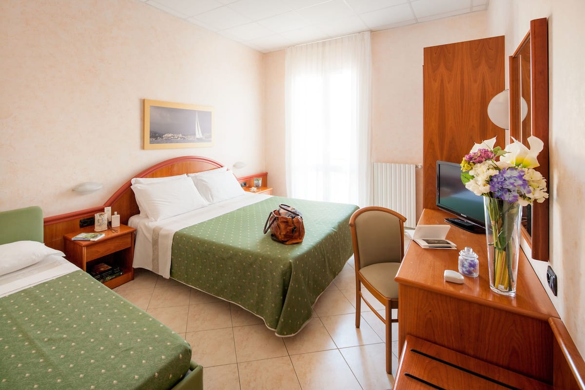 A hotel room with two beds, a desk with a TV, a chair, a nightstand, and a window with curtains.