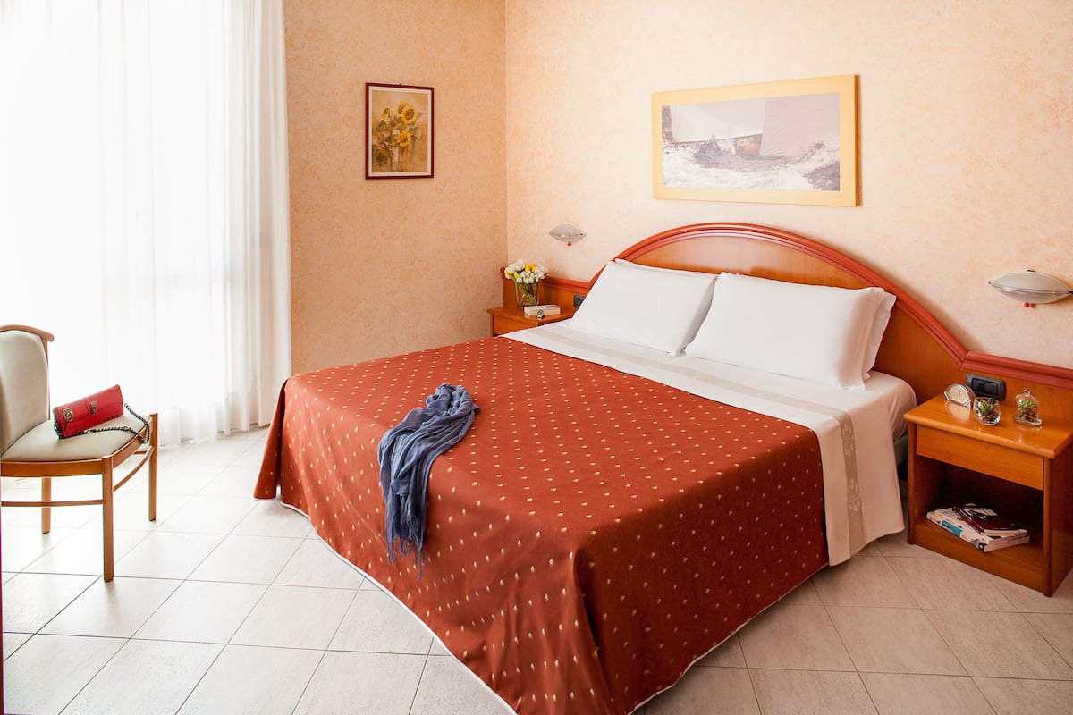 A hotel room with a large bed, a chair, a nightstand, and a wall with two framed pictures.