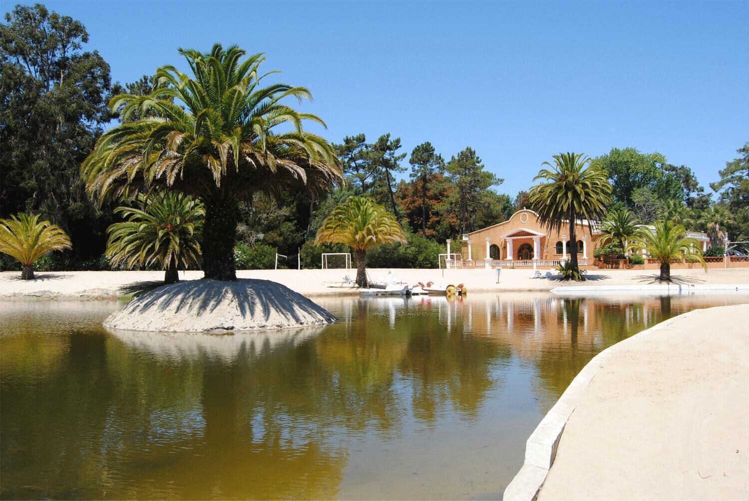 Un entorno tranquilo junto al lago, con palmeras, una playa de arena y un edificio con una entrada de arco característico.