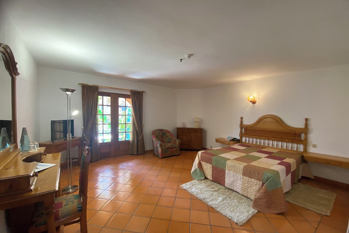 A bedroom with a bed, a desk, a chair, a dresser, and a window with curtains.