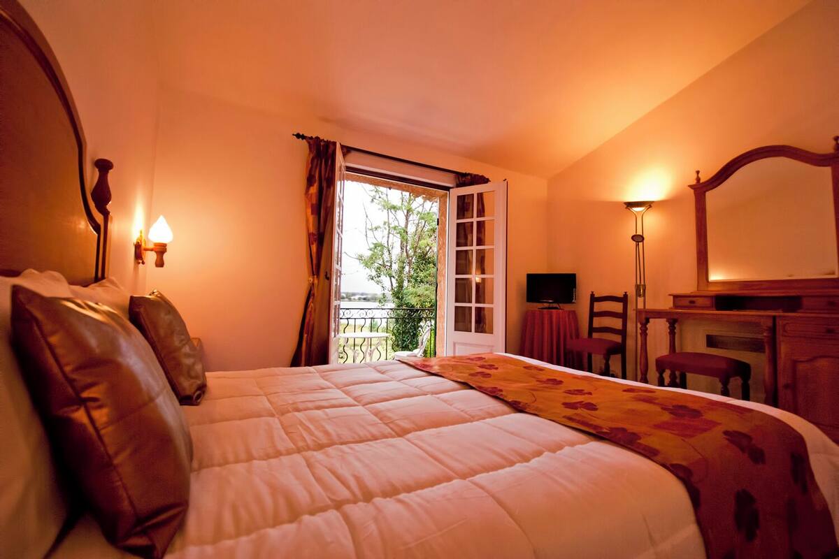 A bedroom with a bed, a desk, a chair, a TV, and a balcony with a view.
