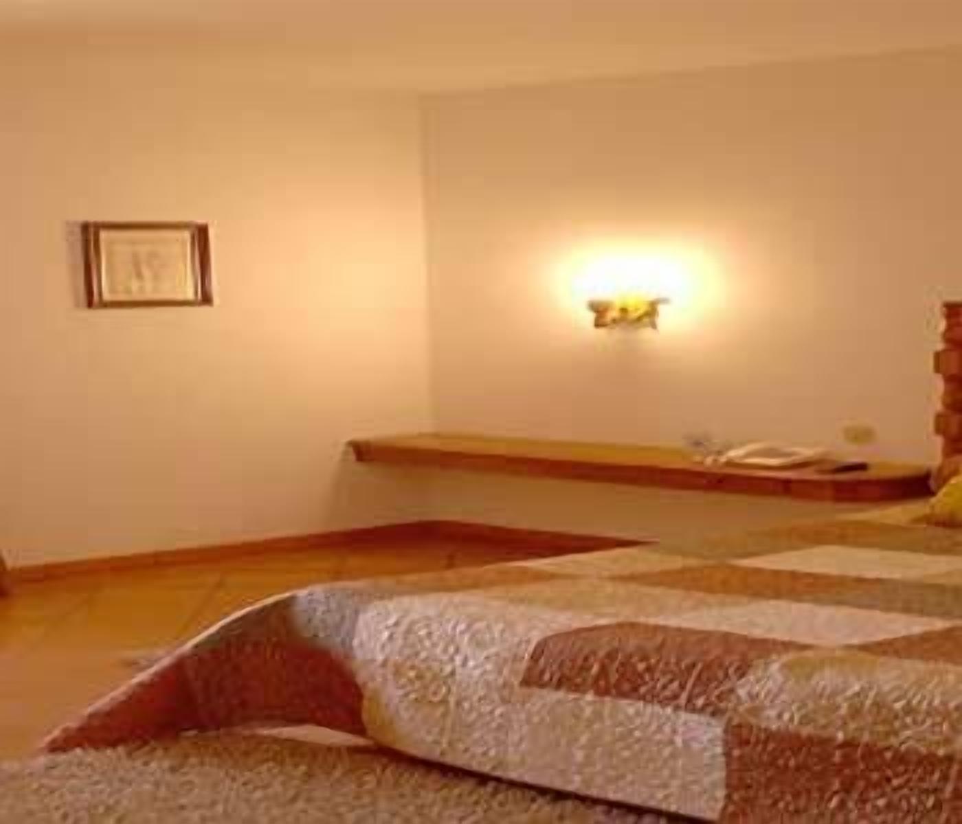 Une chambre à coucher comprenant un lit, une table de chevet, une commode, une lampe fixée au mur et un tableau encadré accroché au mur.