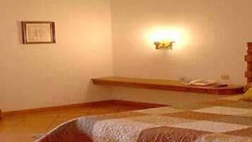 Une chambre à coucher comprenant un lit, une table de chevet, une commode, une lampe fixée au mur et un tableau encadré accroché au mur.