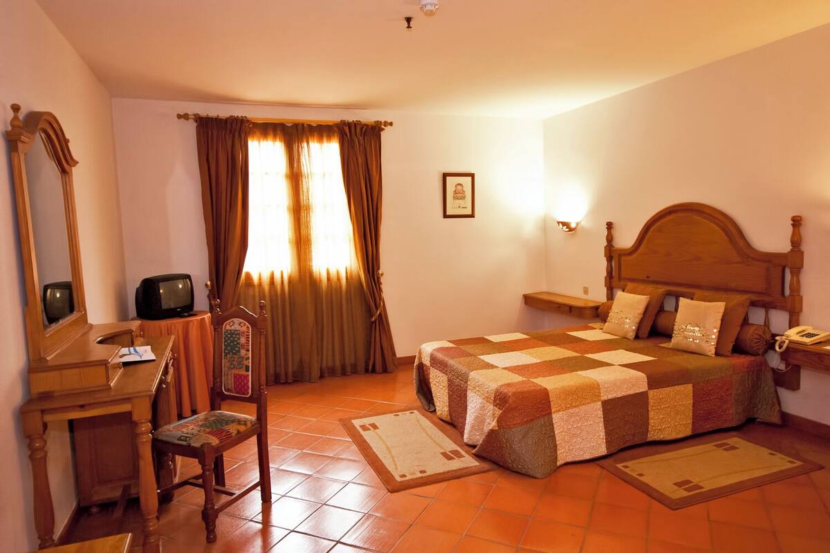 A bedroom with a bed, bedside table, lamp, and a desk with a chair.