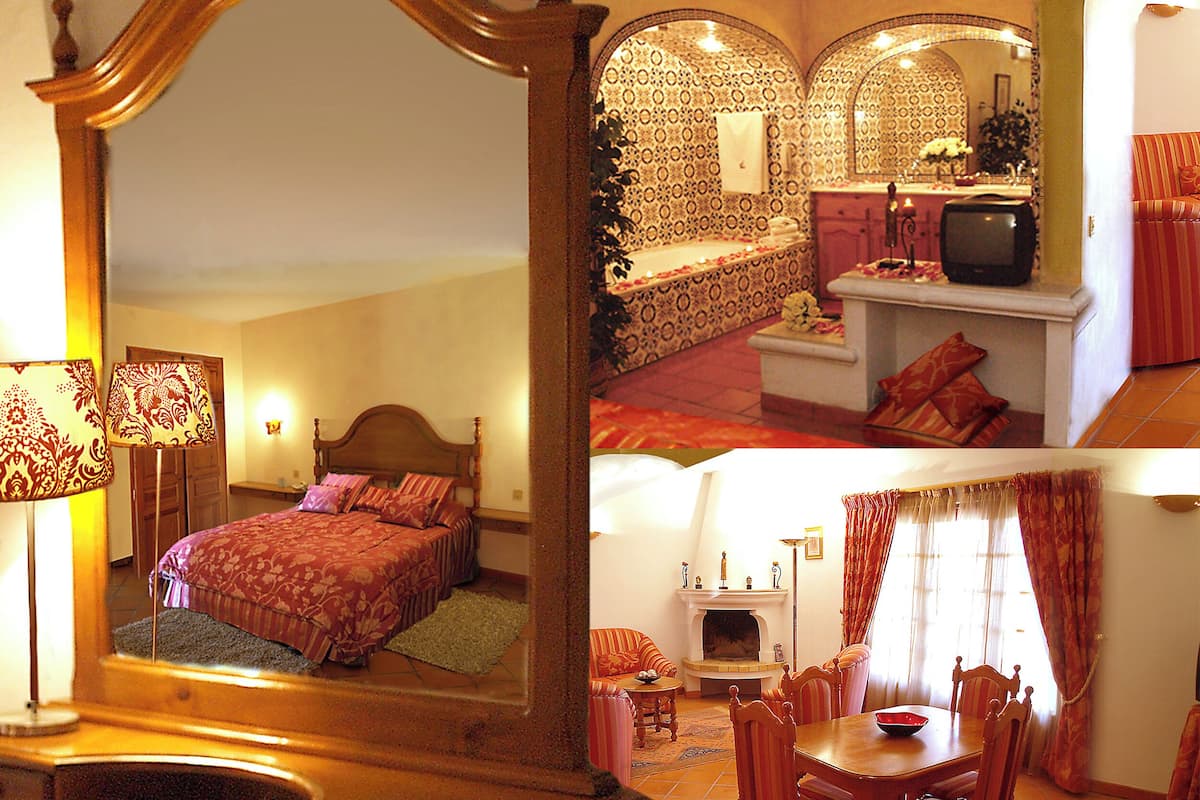 A hotel room with a bed, a sitting area with a fireplace, and a television.